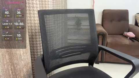 Media: Video of a modern office chair with black mesh backrest and armrests, positioned in a beige-patterned wall, adjacent to a brown leather couch with pink clothes on it.