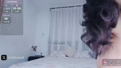 Media: A video of a bedroom with a large bed covered in white linens, a partially visible person with wavy, dark hair, and a digital clock displaying 26:10:50 on the left wall.