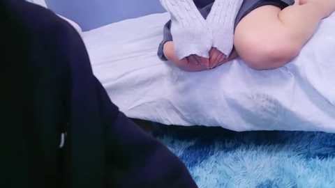 Media: A video shows a woman with fair skin lying on a blue plush carpet, wearing a white knitted sweater, with a glimpse of her bare breast visible.