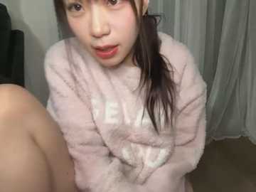 Media: A video of an Asian woman with fair skin, wearing a pink fluffy robe, sitting on a beige carpet. She has long, dark hair tied back, and is looking directly at the camera with a surprised expression.