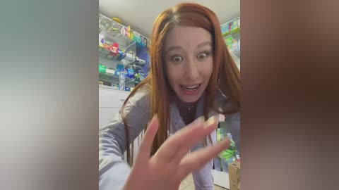 Media: A video of a woman with long red hair, wearing a gray sweater, kneeling in a brightly lit kitchen pantry filled with colorful snacks and drinks. She gestures excitedly with her hands.