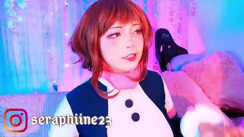 Media: Video of a young Asian woman with shoulder-length auburn hair in cosplay attire, holding a drink, in a colorful, dreamy indoor setting.