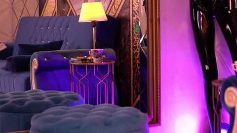 Media: Video of a stylish, dimly lit living room with a blue velvet sofa, tufted ottoman, gold geometric side table, and an ornate mirror reflecting purple lighting.