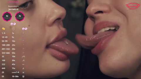 Video of two women, one with fair skin, the other with darker skin, sharing a kiss, both with slightly parted lips and tongues visible, in a dimly lit setting.