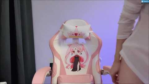 Media: Video of a pink and white gaming chair with a cartoon character design, featuring a girl with pink hair and a red heart-shaped mouth. A person in a white shirt is partially visible on the right.