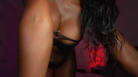 Media: A close-up video of a black woman with wet, dark hair, wearing a black, sheer bra and panties, her hand touching her breast, against a dark purple background.