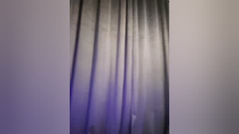 Media: A video of a dark gray curtain with a subtle gradient of light purple at the top, set against a plain white wall. The curtain's texture is smooth and slightly creased, creating a soft, diffused lighting effect.