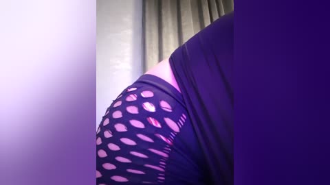 Media: Video of a close-up view of a woman's arm, showing a black sleeve with large cut-out heart shapes revealing skin, against a purple and beige background.