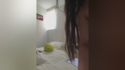 Media: A video of a dimly lit, cluttered bedroom with a green pillow on a white bed, a blurry person with long hair in the foreground, and a colorful poster on the wall.