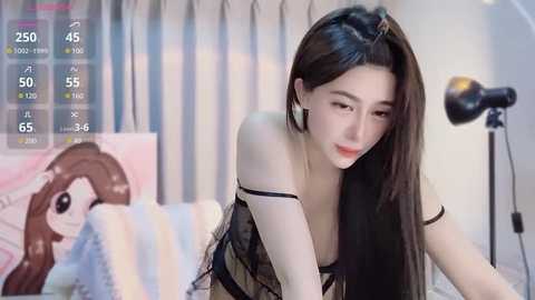 Media: Video of a slender East Asian woman with long black hair, wearing a black lace lingerie top, leaning forward in a bedroom with a striped bedspread, a poster, and a studio light.