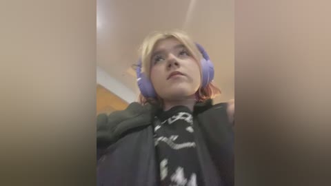 Media: A video of a young person with fair skin, wearing purple headphones, a black jacket, and a graphic T-shirt, taken from a low angle, with a blurred background.