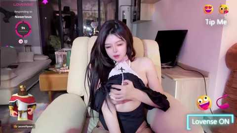 Media: A video of an Asian woman in a black lace bra, sitting in a beige armchair, holding a smartphone, surrounded by a modern living room.