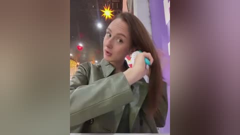 Media: Video of a woman with long brown hair, wearing a green leather jacket, holding a phone to her ear, standing in a room with Christmas lights and a blurred background.