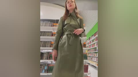 Media: Video of a tall, slim woman in a green trench coat standing in a bright, modern bookstore with shelves of books and green accents.