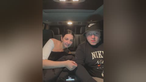 Media: Video of two people in a dimly-lit car, a woman with long dark hair in a white top, and a man in a black Nike hoodie, both smiling.