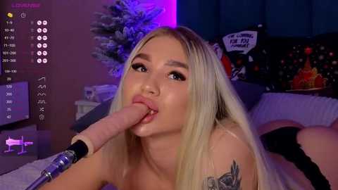 Media: Video of a young blonde woman with long hair, wearing a black top, performing oral sex on a large, erect penis, in a dimly-lit room with a Christmas tree and decorations.