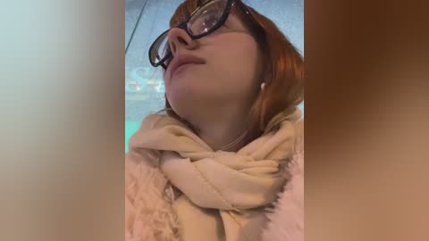 Media: A video of a young woman with fair skin, red hair, and glasses, wearing a beige scarf and a fluffy pink jacket, looking up, with a blurred background.