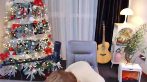 A video of a cozy living room with a decorated Christmas tree, a guitar, and a fireplace, featuring a person in a white hat and sweater in the foreground.