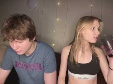 Media: Video of a young couple in a dimly lit room; the girl, with long blonde hair, wears a black sports bra and looks pensive, while the boy, with short brown hair, gazes downward in a blue t-shirt.