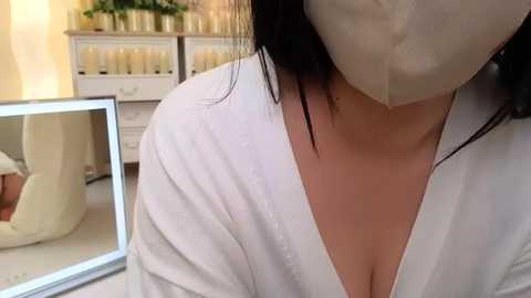 Video of a woman in a white robe, face masked, in a spa setting with candles, reflecting in a mirror.