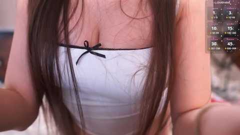 Video of a woman with long brown hair wearing a white tube top with a black bow, showing cleavage, and an overlay of a gaming stream with chat.