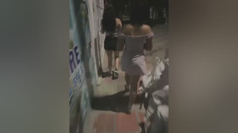 Media: A video captures a woman in a grey top and shorts being restrained by two men in a dimly lit alley. One man has his arm around her neck, and the other holds her arm. The background is blurry, with a wall and indistinct objects.