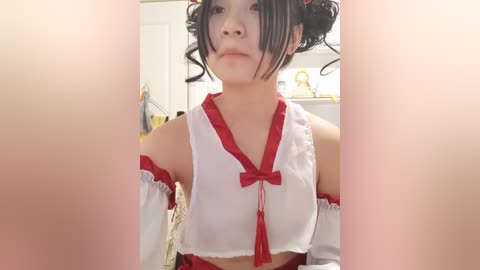 Media: Video of an East Asian woman in a revealing white and red cosplay outfit with detached sleeves, wearing a red bow and black hair in buns. Background includes a white door and furniture.