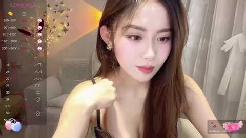 Media: Video of an Asian woman with long, straight brown hair and fair skin, wearing a sleeveless top, smiling and adjusting her hair. Background features a blurred, cozy room with white curtains and a decorative plant.