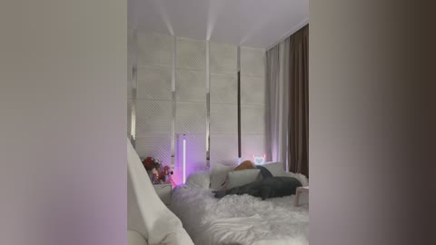 Media: Video of a minimalist, modern bedroom with white walls, a white bed with fluffy white blanket, and a white lattice screen divider. The room is softly lit with purple and white LED lights, and there is a large window with brown curtains.