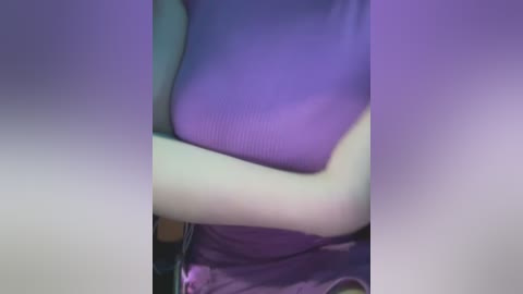 Media: A blurred, purple-hued video of a person with light skin, wearing a form-fitting, sleeveless top, sitting with crossed arms, partially visible in the frame.