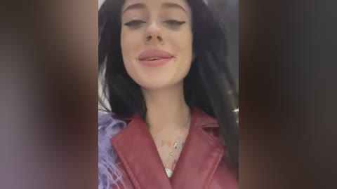 Media: Video of a young woman with long, dark hair and light skin, wearing a red leather jacket and a silver necklace. She has a closed-mouth smile.