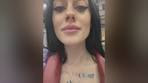 Media: Video of a young woman with pale skin, long black hair, and dark eyeliner. She wears a red jacket and has a nose ring, a lip piercing, and a tattoo with \"LIVE\" and \"HOPE?\" on her chest.