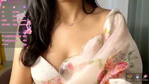 Media: A close-up video of a woman with long, dark hair, wearing a white floral blouse and a delicate gold necklace. The background shows a chat window with various messages and emojis.