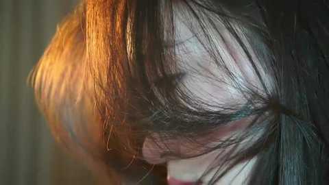 Media: A close-up video of a young person with long, tousled dark hair, partly illuminated by warm light, creating a dramatic, textured effect.