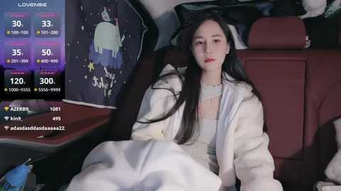 Media: A video of a young East Asian woman with long black hair, wearing a white robe, asleep in a car, with a live-streaming overlay displaying viewer metrics.