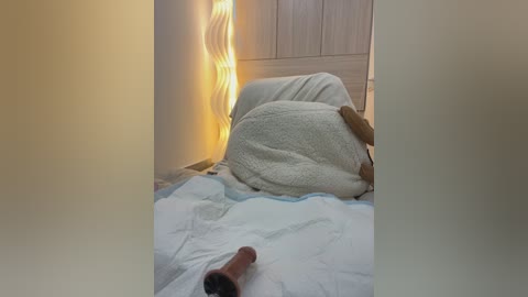 Media: A video of a woman, possibly of African descent, lying on a bed with a white pillow and blanket, holding a lit candle, with a dildo on the bed, in a dimly lit room.