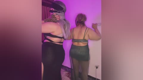 Media: Video of two women in BDSM gear, one with leopard print mask and black corset, the other with green lingerie and sheer stockings, in a dimly lit room.