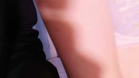 Media: A close-up video of a person's upper thigh, with visible tan lines, likely indicating a bikini area, and a hint of a dark garment on the left side. The background is blurred, showing a light-colored wall.