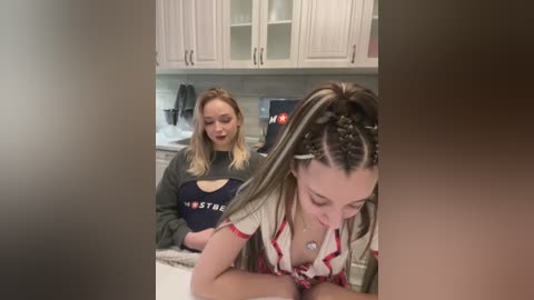 Media: Video of two women in a modern kitchen: one with blonde hair, wearing a \"Nestl\u00e9\" shirt, and another with long, braided hair, leaning over a counter.