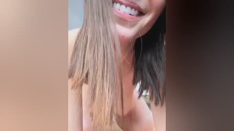 Media: Video of a smiling woman with long, straight, light brown hair partially covering her face, showing off a light skin tone and small, silver hoop earrings.