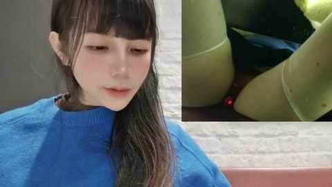 Media: Video of a young Asian woman with long dark hair in a blue sweater, looking down in a soft, contemplative manner. Close-up inset shows her bare legs and a red stain on her thigh.