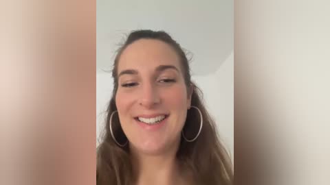 Media: A video of a smiling woman with fair skin, long brown hair, and large silver hoop earrings, set against a plain white background.