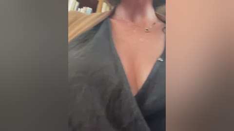 Media: A close-up video of a woman's cleavage in a low-cut black dress, with a gold necklace visible, partially blurred background.