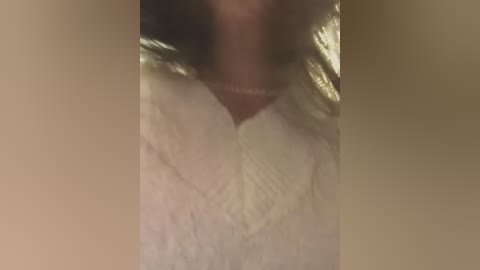 A blurry video of a person wearing a white, textured shirt. The image is grainy and out of focus, making it difficult to discern specific details or features.