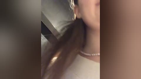 Media: A blurred video of a woman's profile, with long brown hair flowing over her shoulder. She wears a pearl necklace. The background shows a blurred metal object.