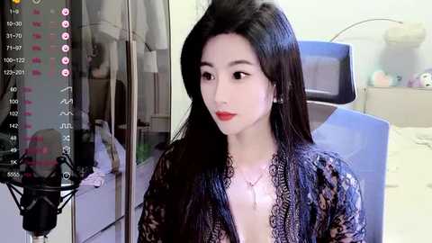 Media: A video of a slender East Asian woman with long black hair, fair skin, and red lipstick, wearing a lace robe, seated in a medical examination room with a digital scale and a bed in the background.