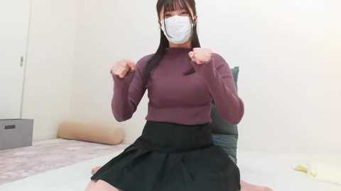 Media: Video of an East Asian woman in a maroon turtleneck, black skirt, and face mask, striking a boxing pose in a minimalist, beige room with a beige rug.