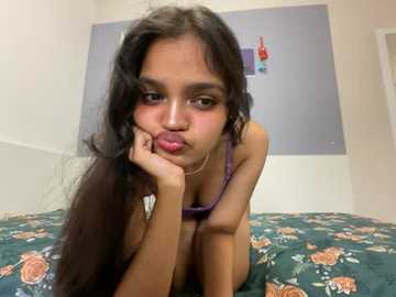 Media: Video of a young South Asian woman with long, dark hair, wearing a purple tank top, lying on a floral-patterned bed, making a pouty face.