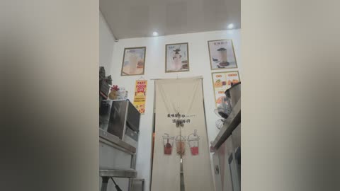 Video of a dimly lit, compact kitchenette with white walls and three framed posters. The room features a sink, a refrigerator, and a small table.