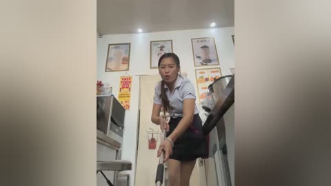 Media: A video of an Asian woman in a white shirt and black skirt, standing near a cash register in a clean, brightly lit coffee shop with framed posters and red \"50% off\" signs on the wall.